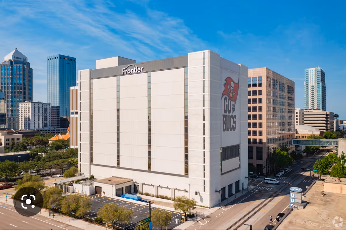 A tall white modern building labeled Frontier along a city street with a large Buccaneers mural.