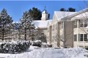 Snow-covered senior living facility exterior with beige buildings, trees, and a clock tower.