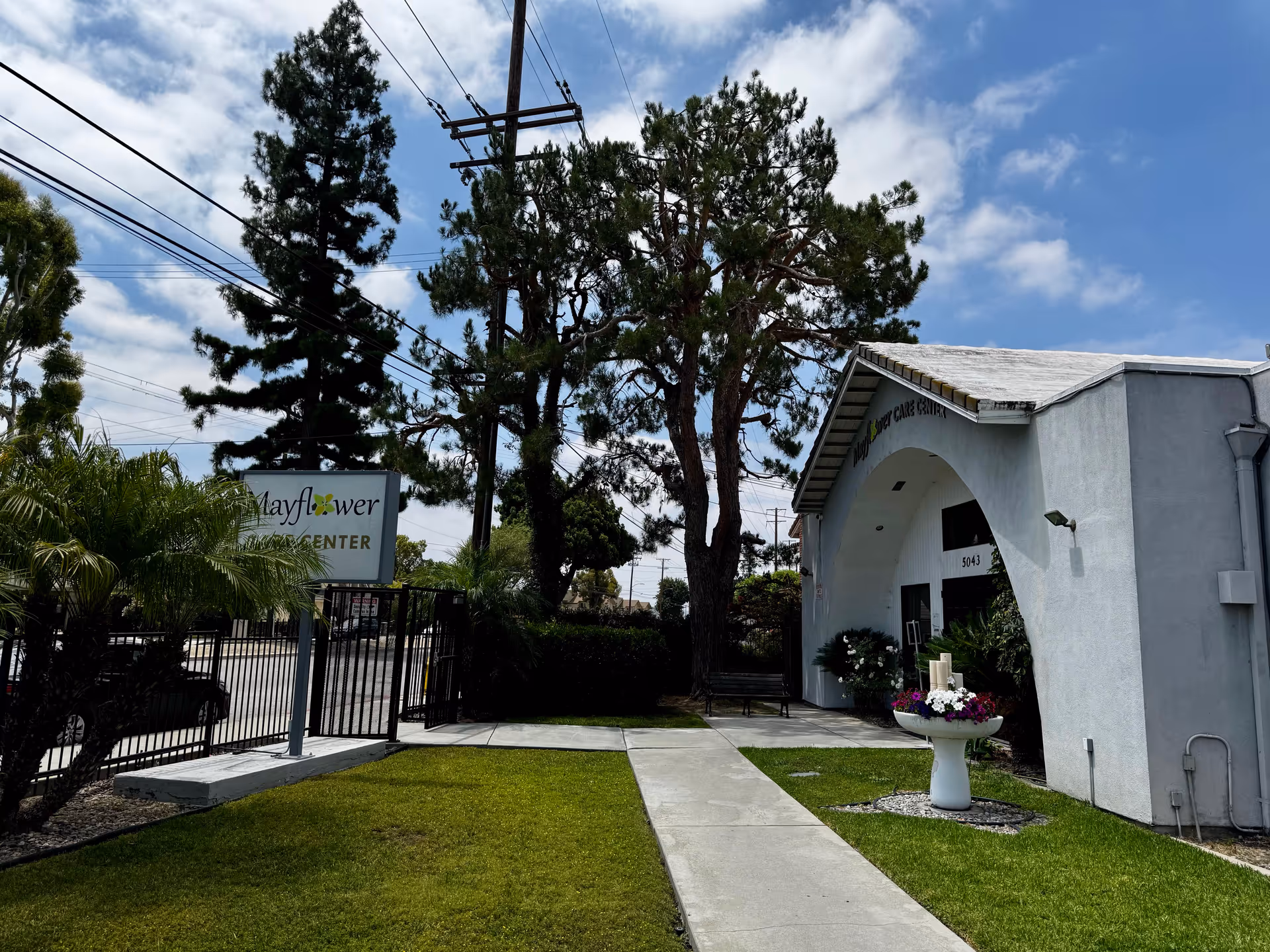 Exterior view of Mayflower Care Center entrance with sign, gate, and landscaping.