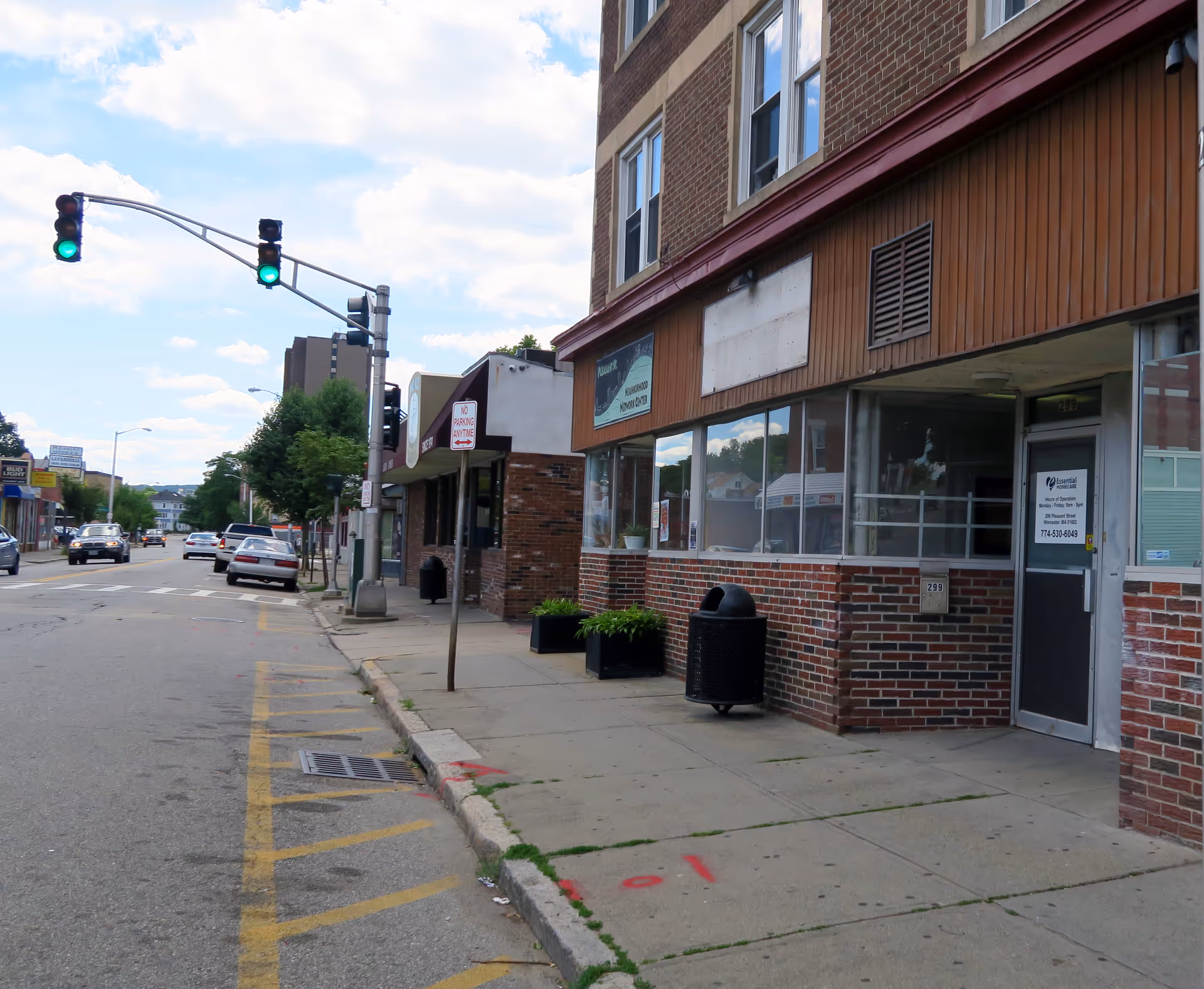 Street view of a brick storefront building with sidewalk, windows, and a traffic light.