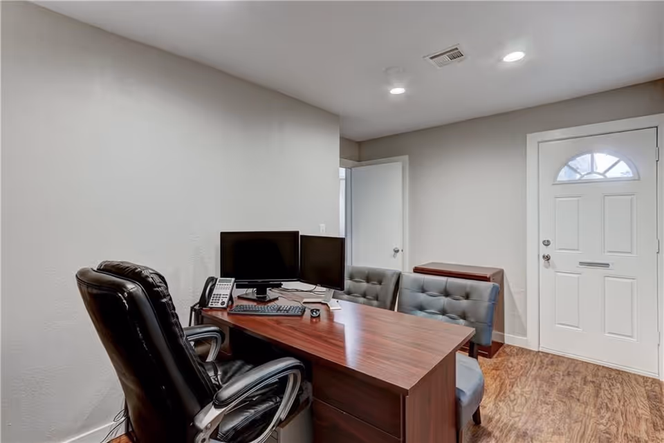 Office space with a desk, dual monitors, phone, leather chair, and a front door.