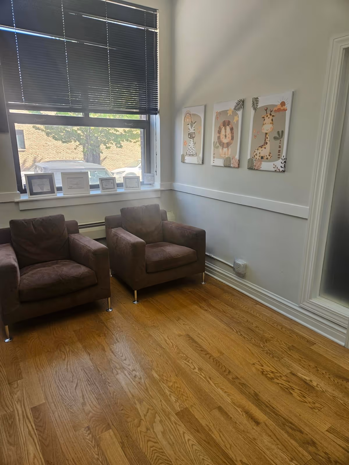 Senior living facility lounge with two brown chairs, window blinds, and animal-themed wall art.