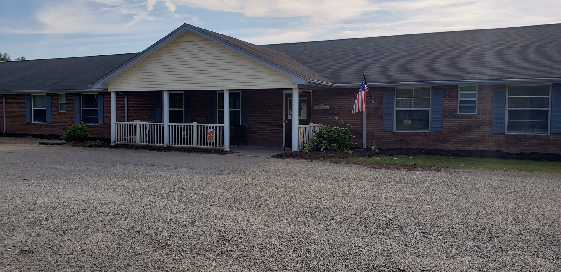Pinewood Manor Assisted Living building front view with brick exterior, porch, and American flag.