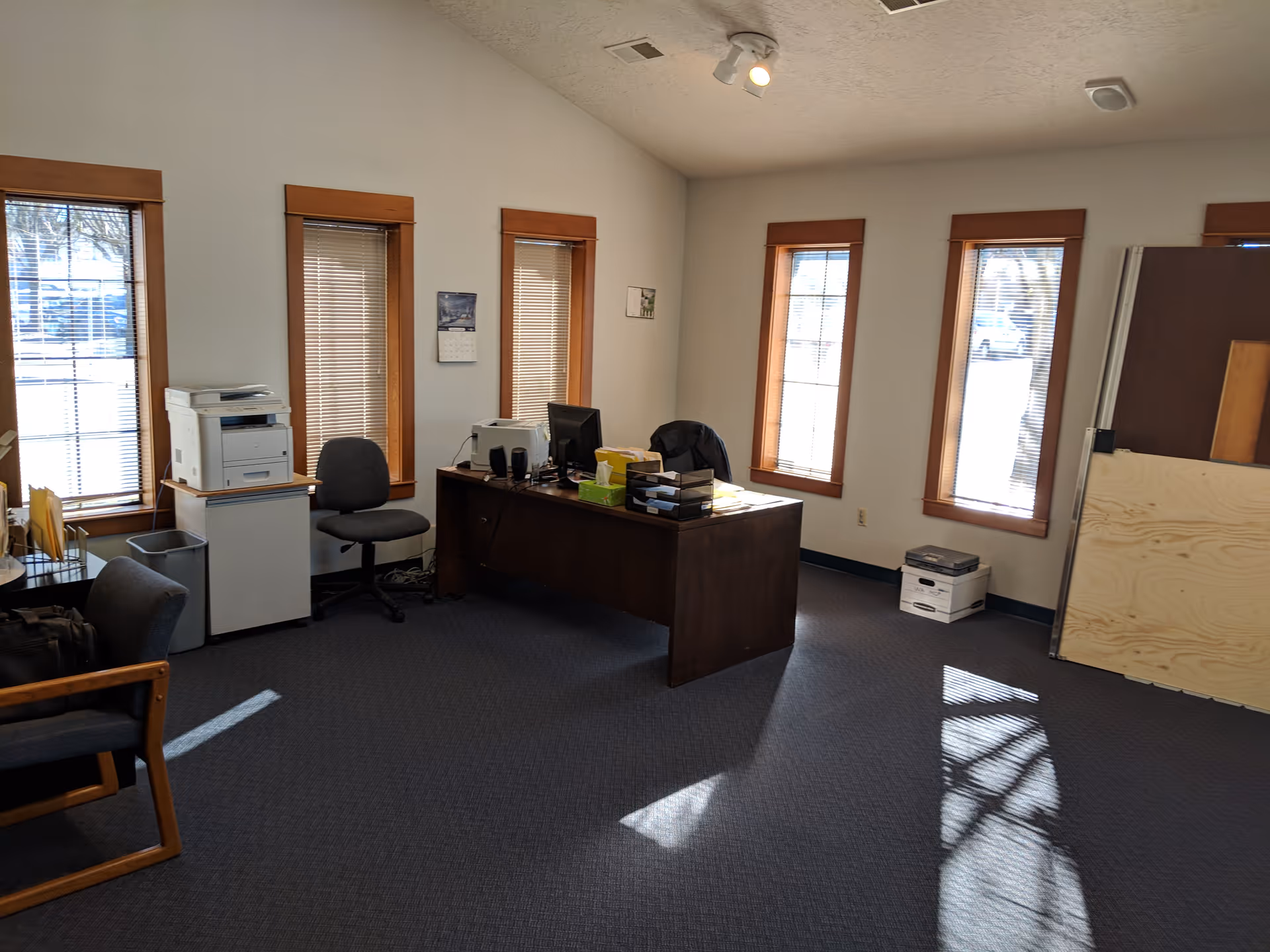 Office area with desk, computer, printer, chairs, and windows with blinds.