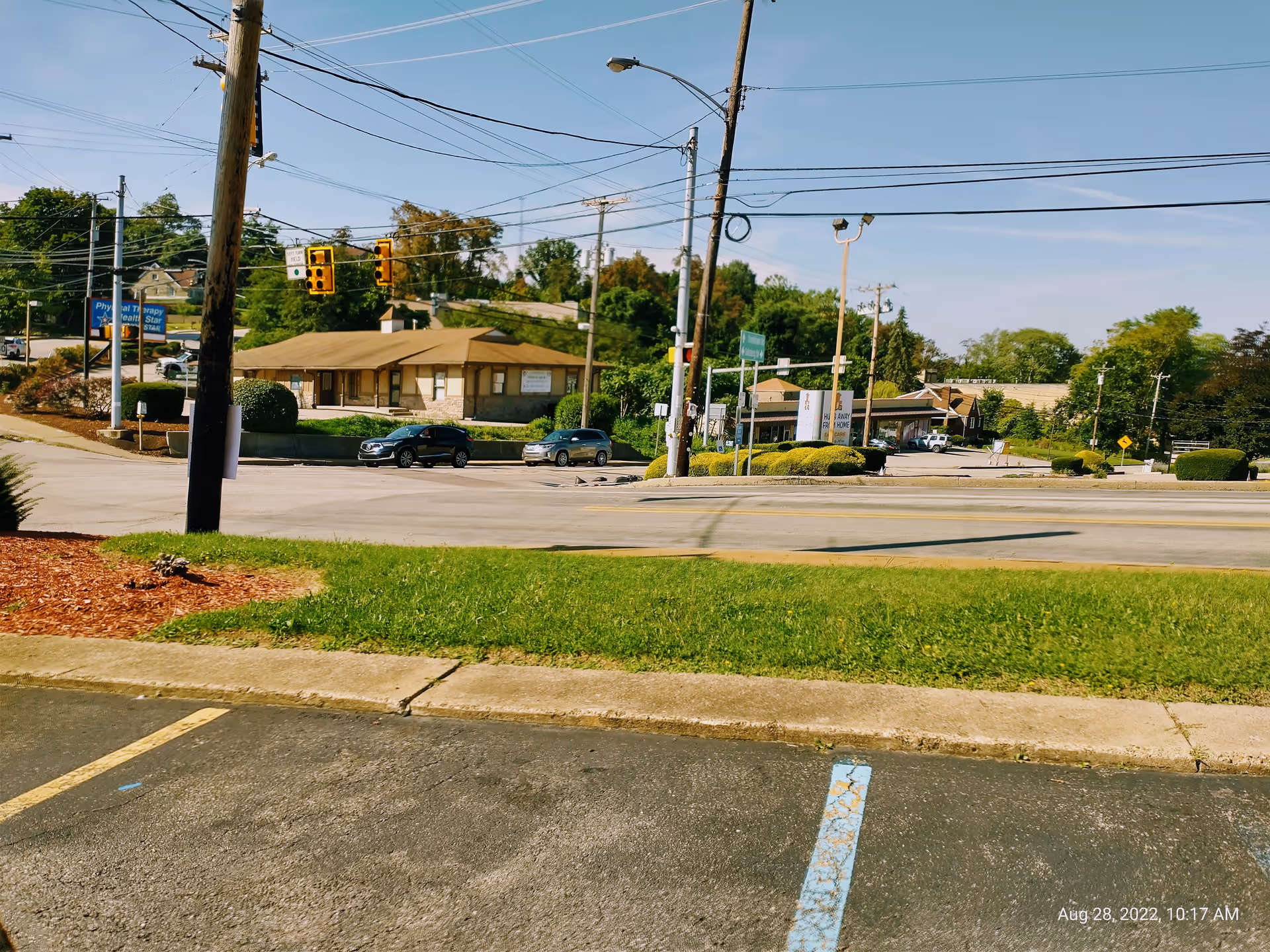 Wide street view of a low, tan building across a parking lot with utility poles.
