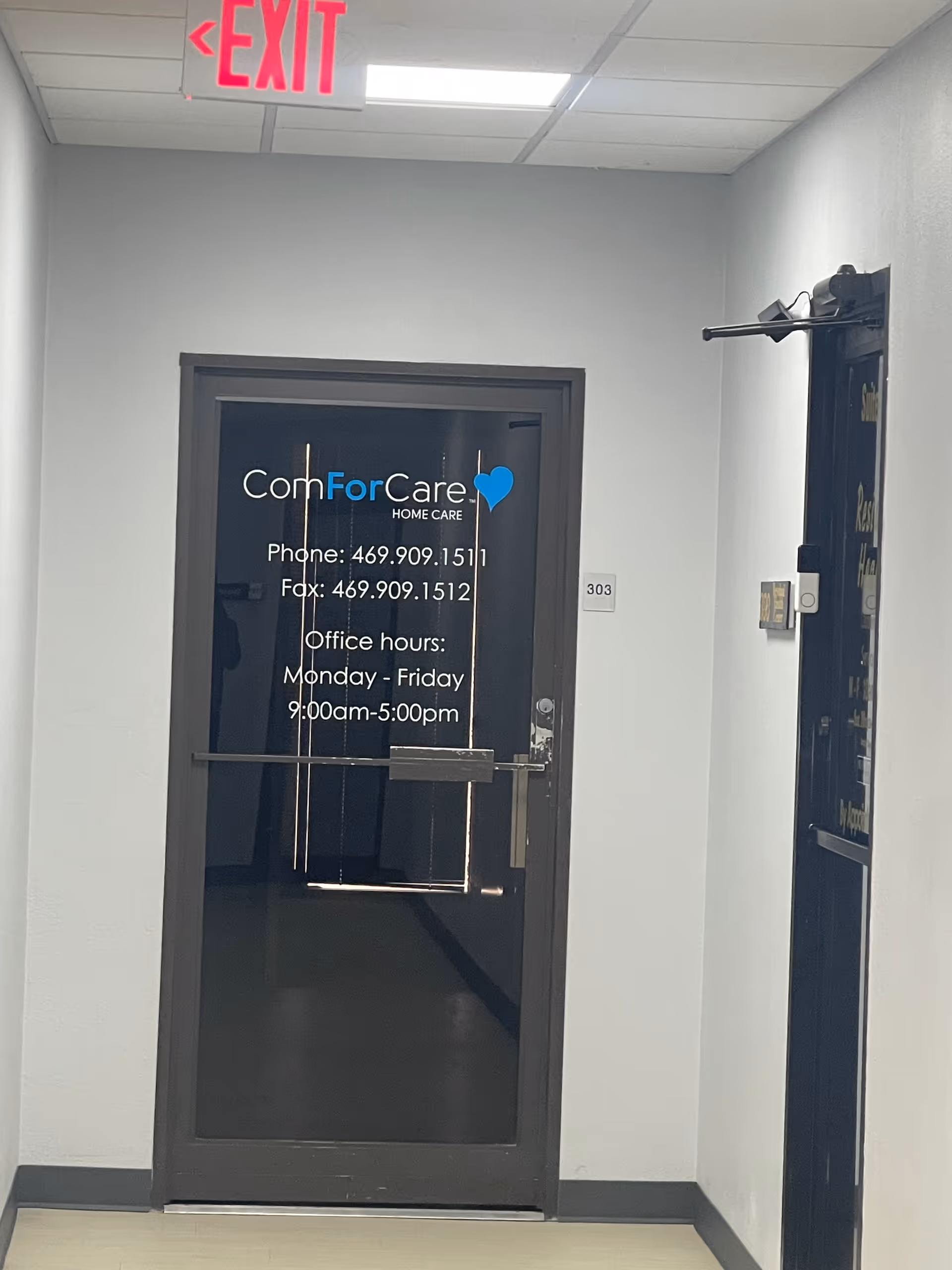 Glass door with ComForCare logo and office hours in a hallway with an exit sign.