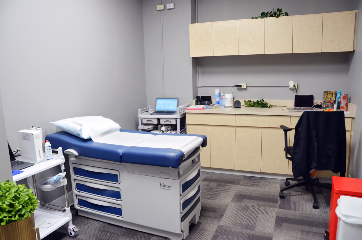 Clinical examination room with a blue medical bed, counters, and assorted equipment.