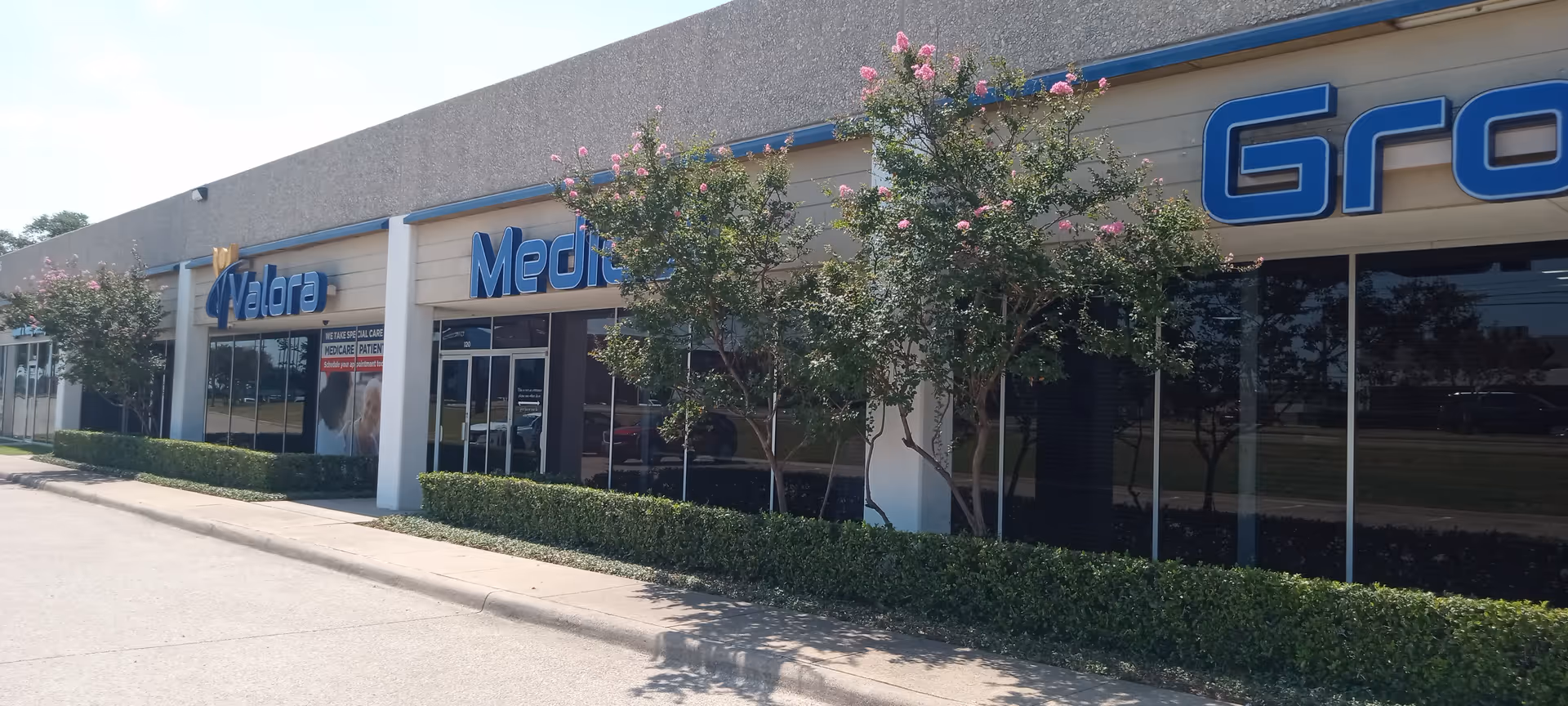 Exterior view of a medical group clinic strip with glass storefronts and trimmed hedges.