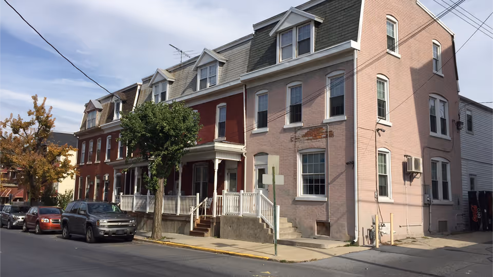 Brick multi-story senior care home with a front porch and parked cars along the street.