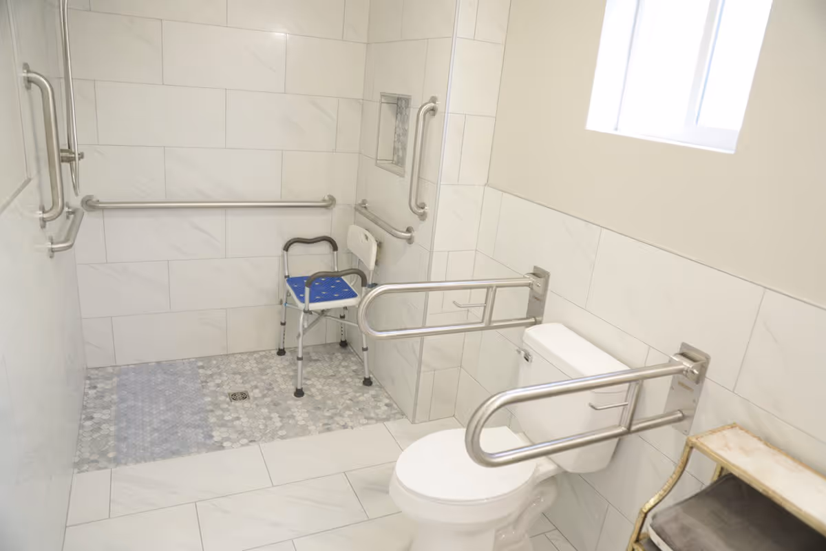 Accessible tiled bathroom with a toilet, shower chair, and grab bars.