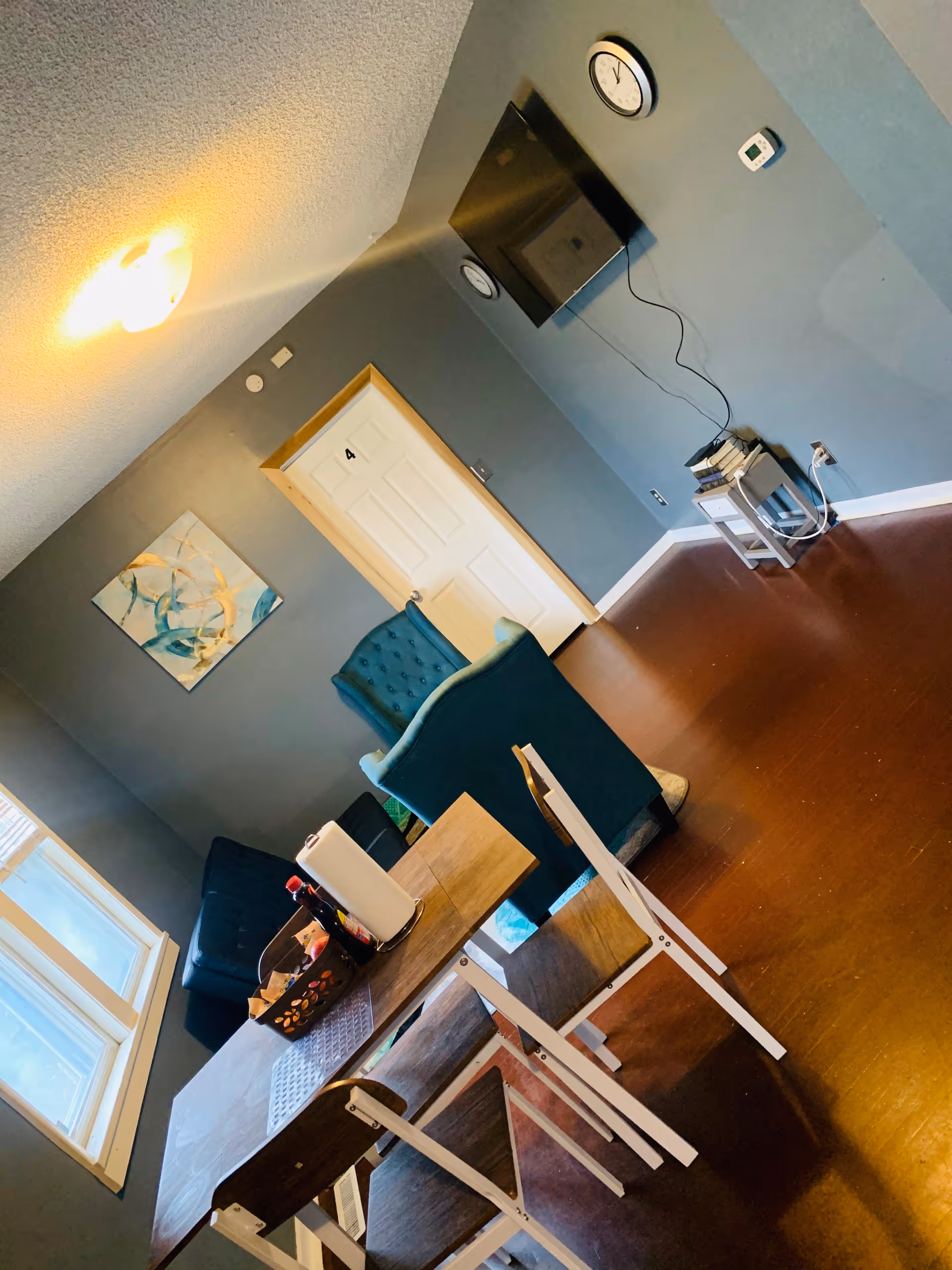 Small common room with a wooden table and folding chairs, teal armchairs, a wall-mounted TV, and a door labeled 4.