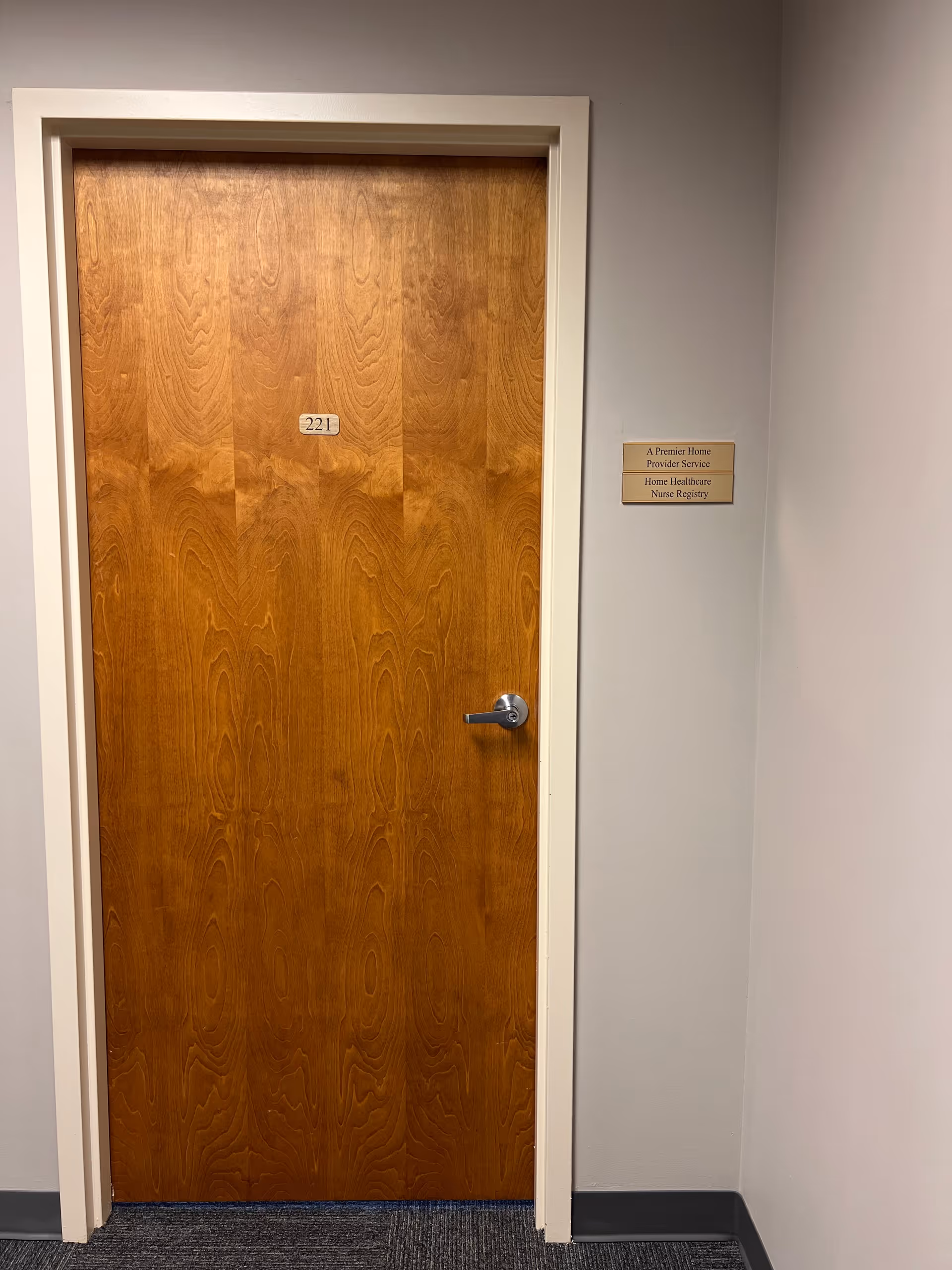 Wooden interior door labeled 221 in a hallway beside a wall plaque.