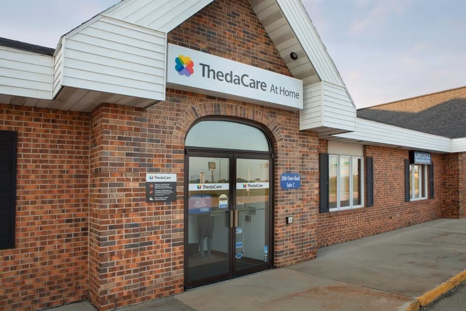 Brick storefront with ThedaCare At Home sign and glass entrance doors.