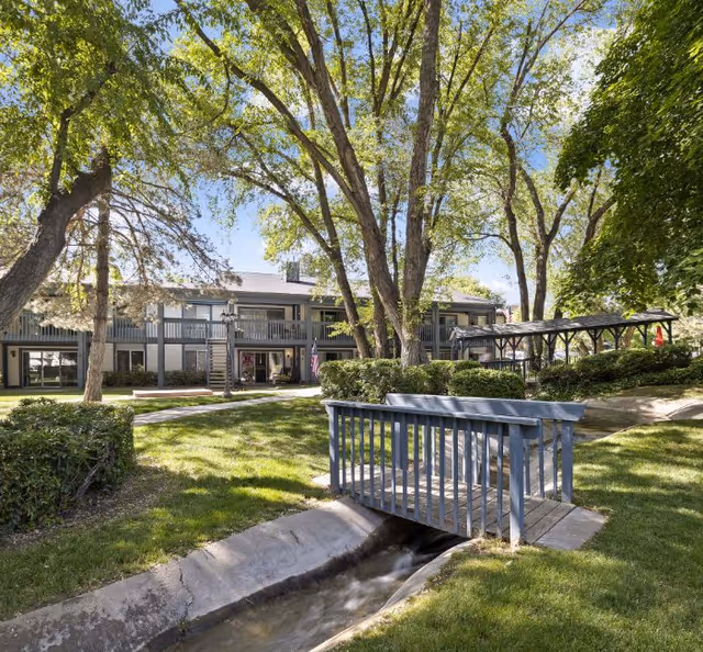 Exterior view of Cove Point Retirement with trees, a footbridge, and a small canal.