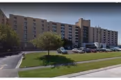 Exterior view of a multi-story senior living center with cars parked along a grassy lawn.