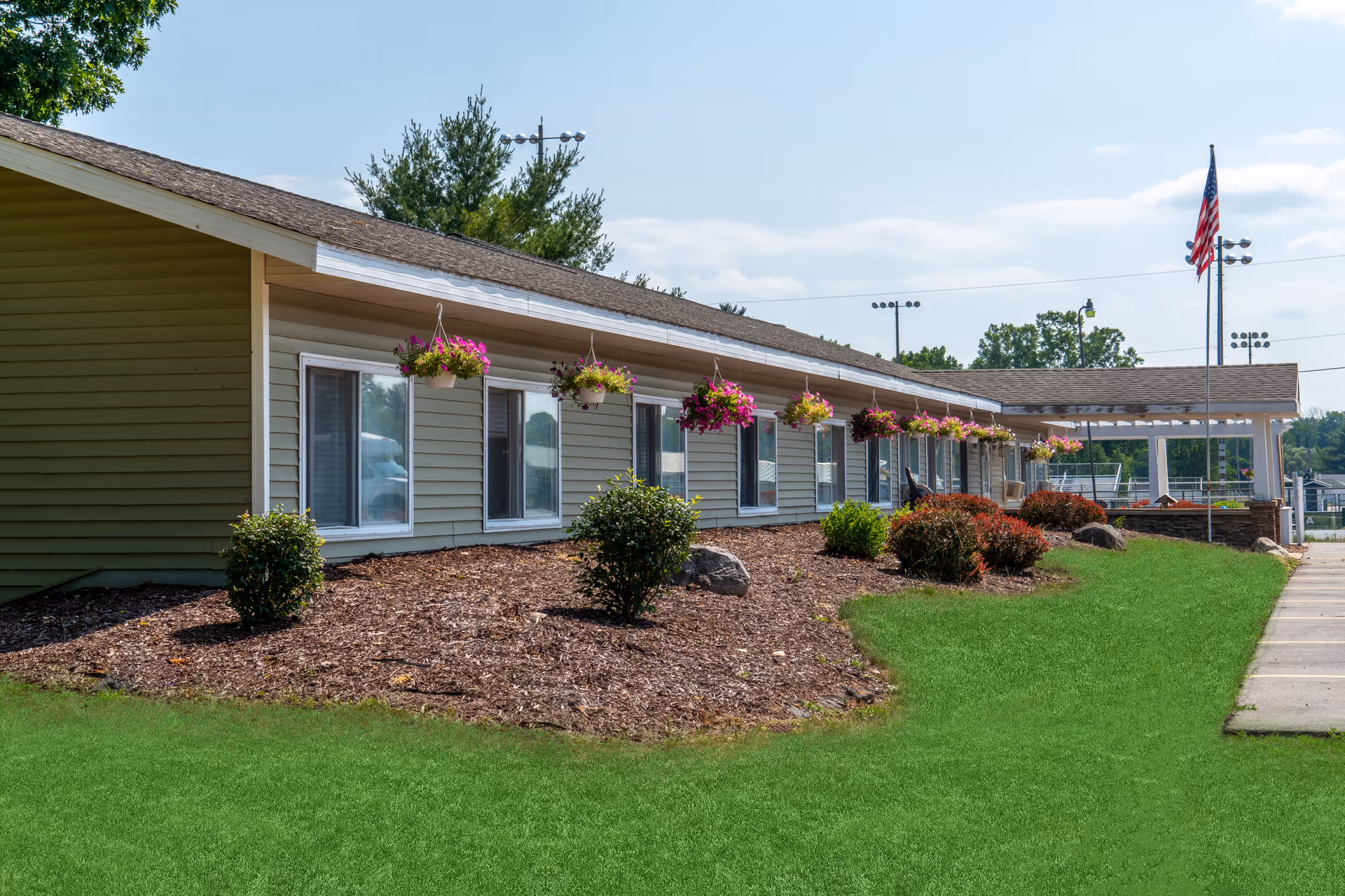 Single-story Americana Seniors building exterior with hanging flower baskets, manicured lawn, and flagpole.