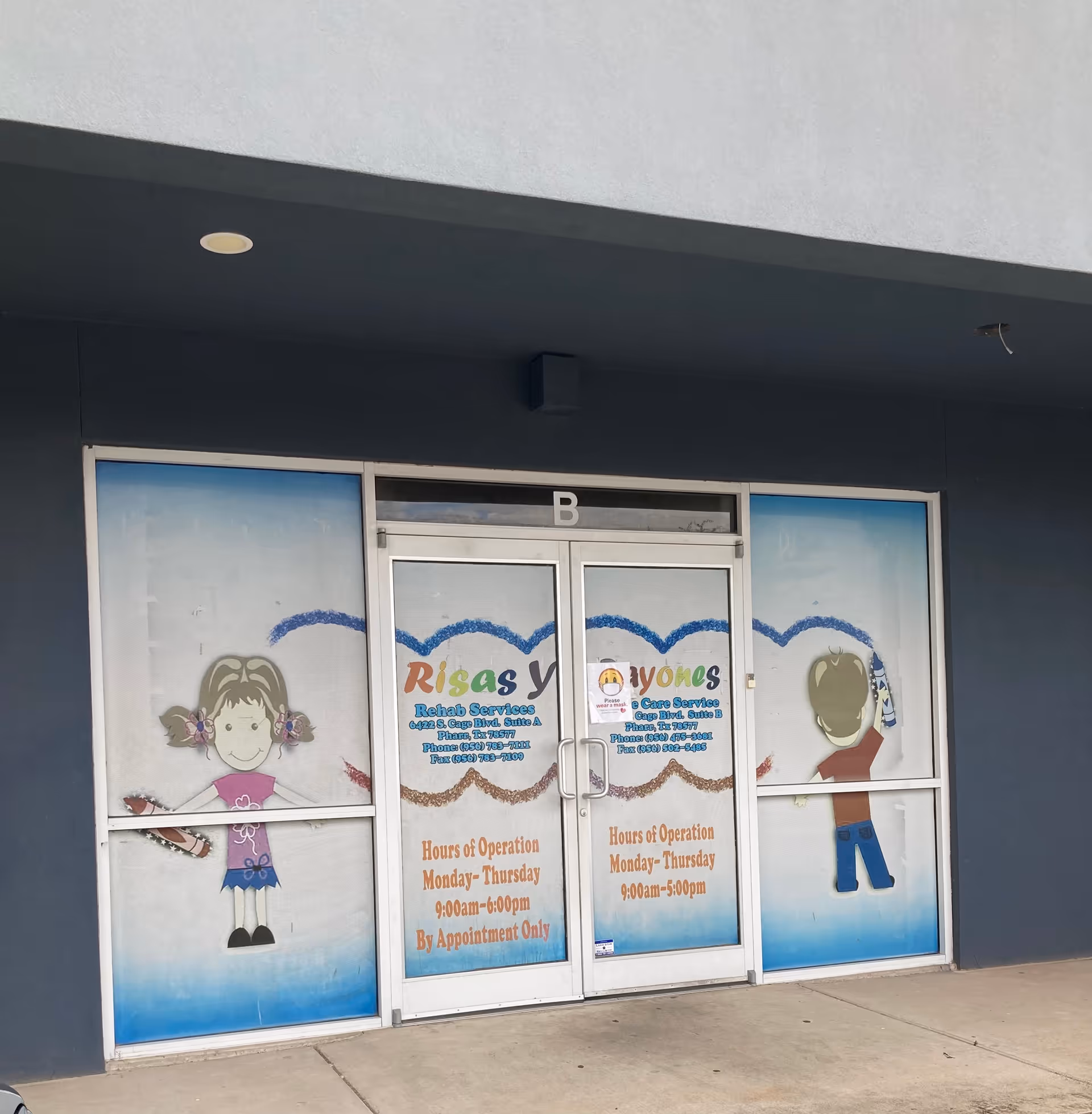 Front entrance of a building with glass doors and colorful Risas Y Rayones signage.