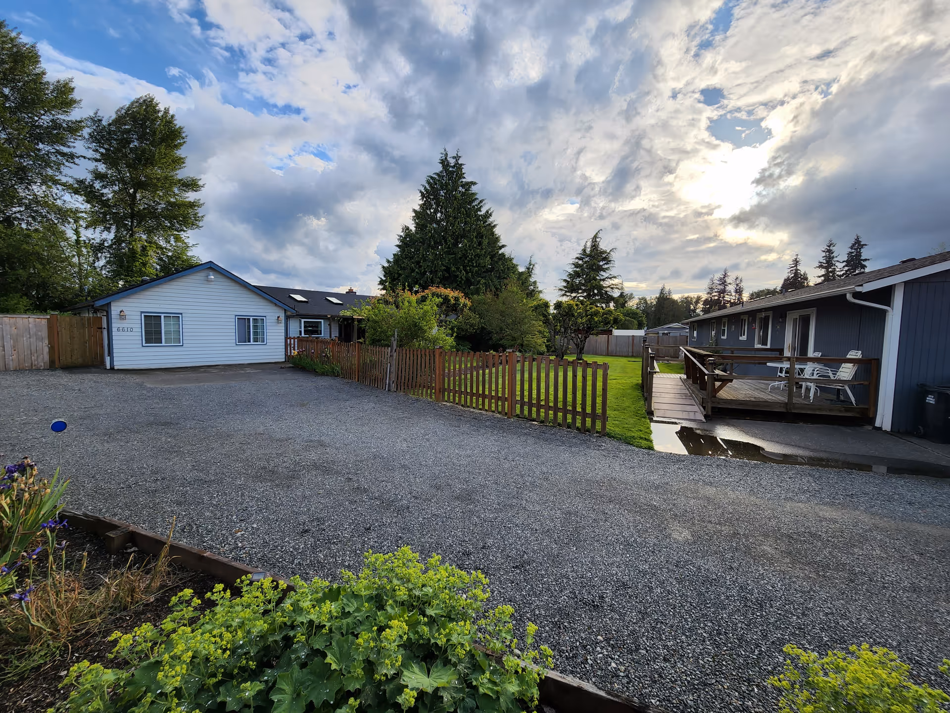 Outdoor scene of a small, single-story facility with a gravel driveway, lawn, and wooden deck.