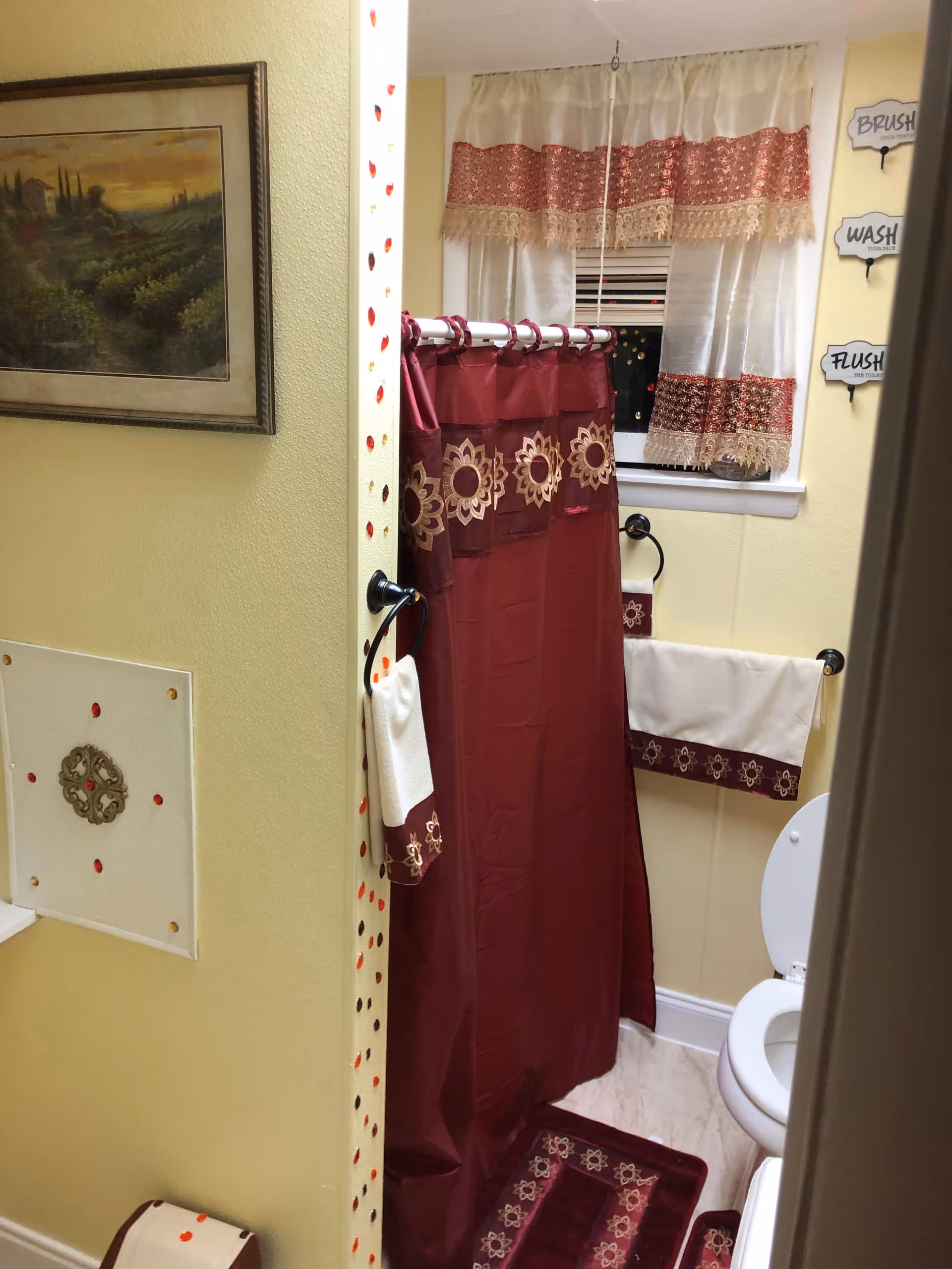 Yellow bathroom with maroon shower curtain, lace window treatment, and toilet