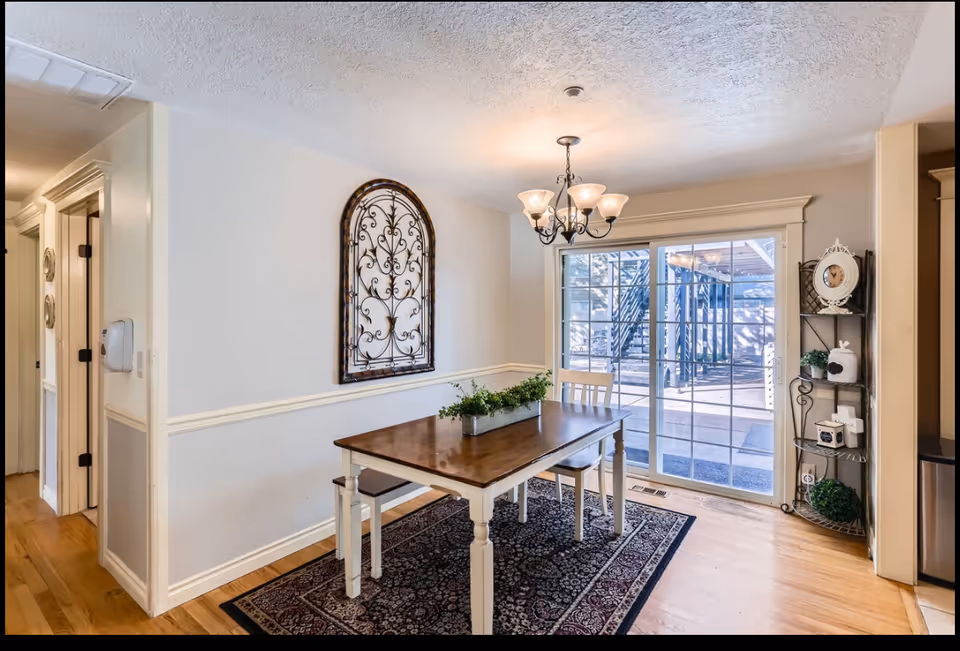 Interior dining room with wooden table, chandelier, sliding glass door, and decorative shelving.