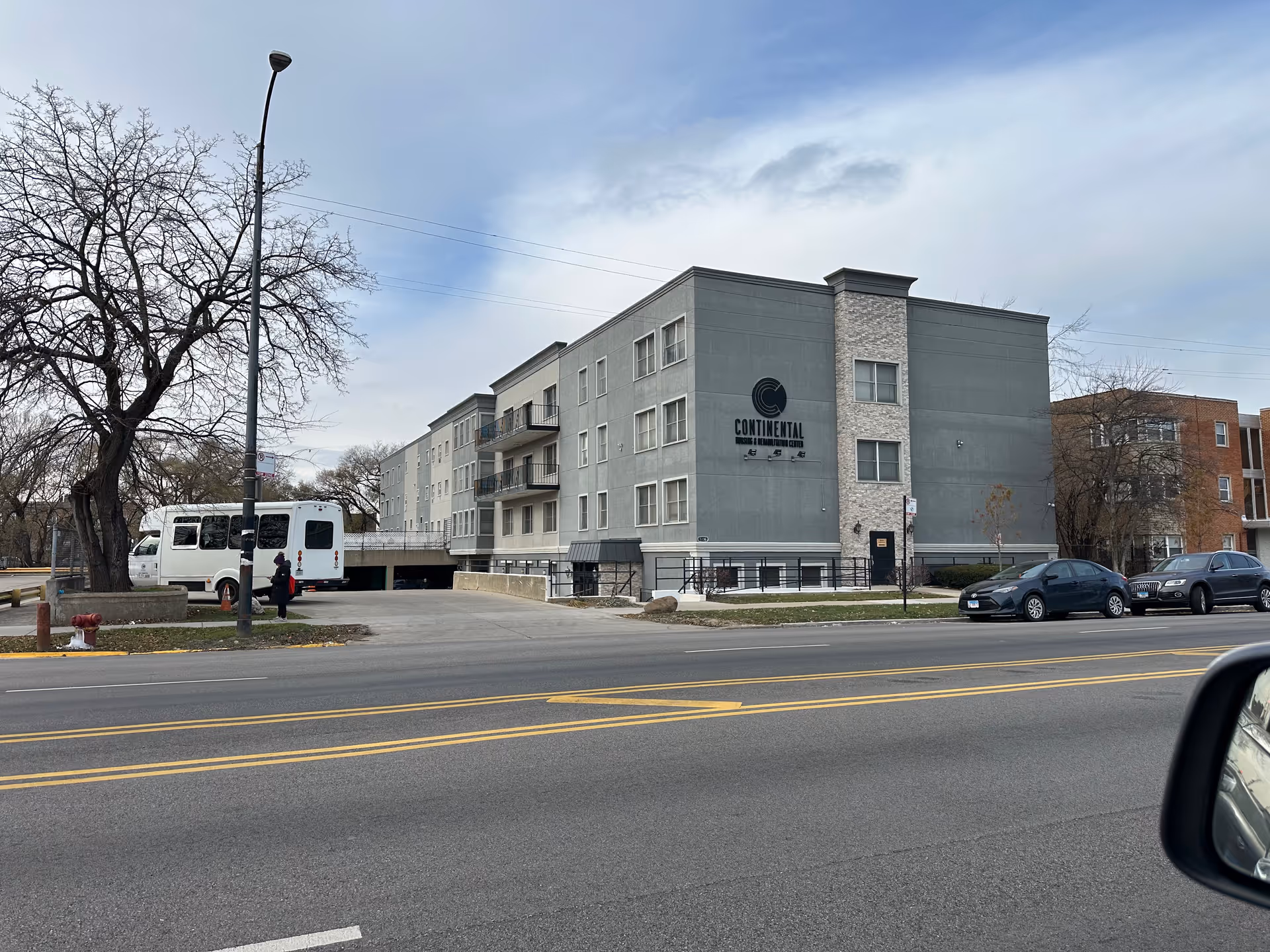 Exterior front view of the Continental Nursing & Rehabilitation Center building on a city street with parked cars and a shuttle bus.