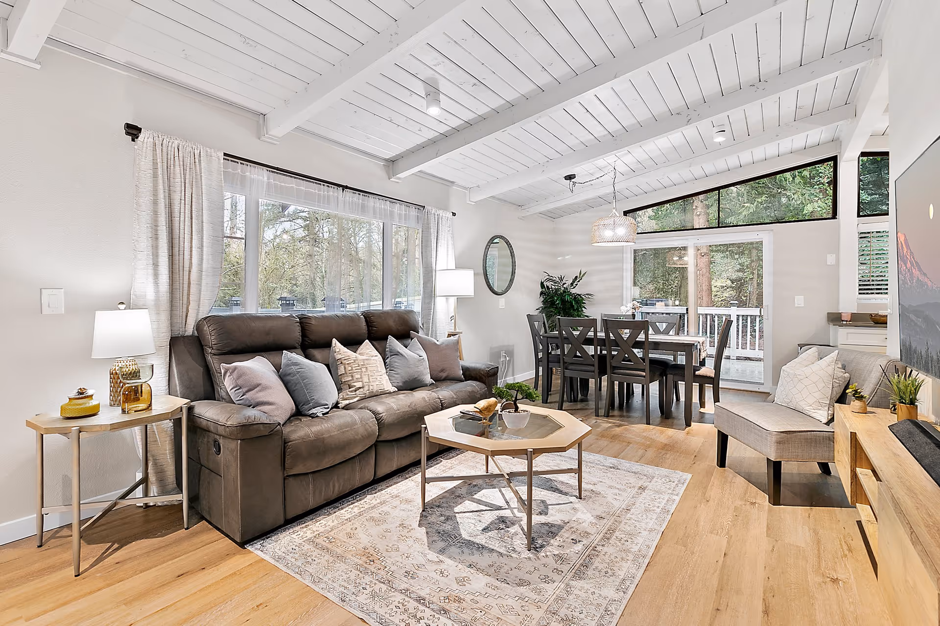 Bright open living room with leather sofa, coffee table, dining area, and large windows.