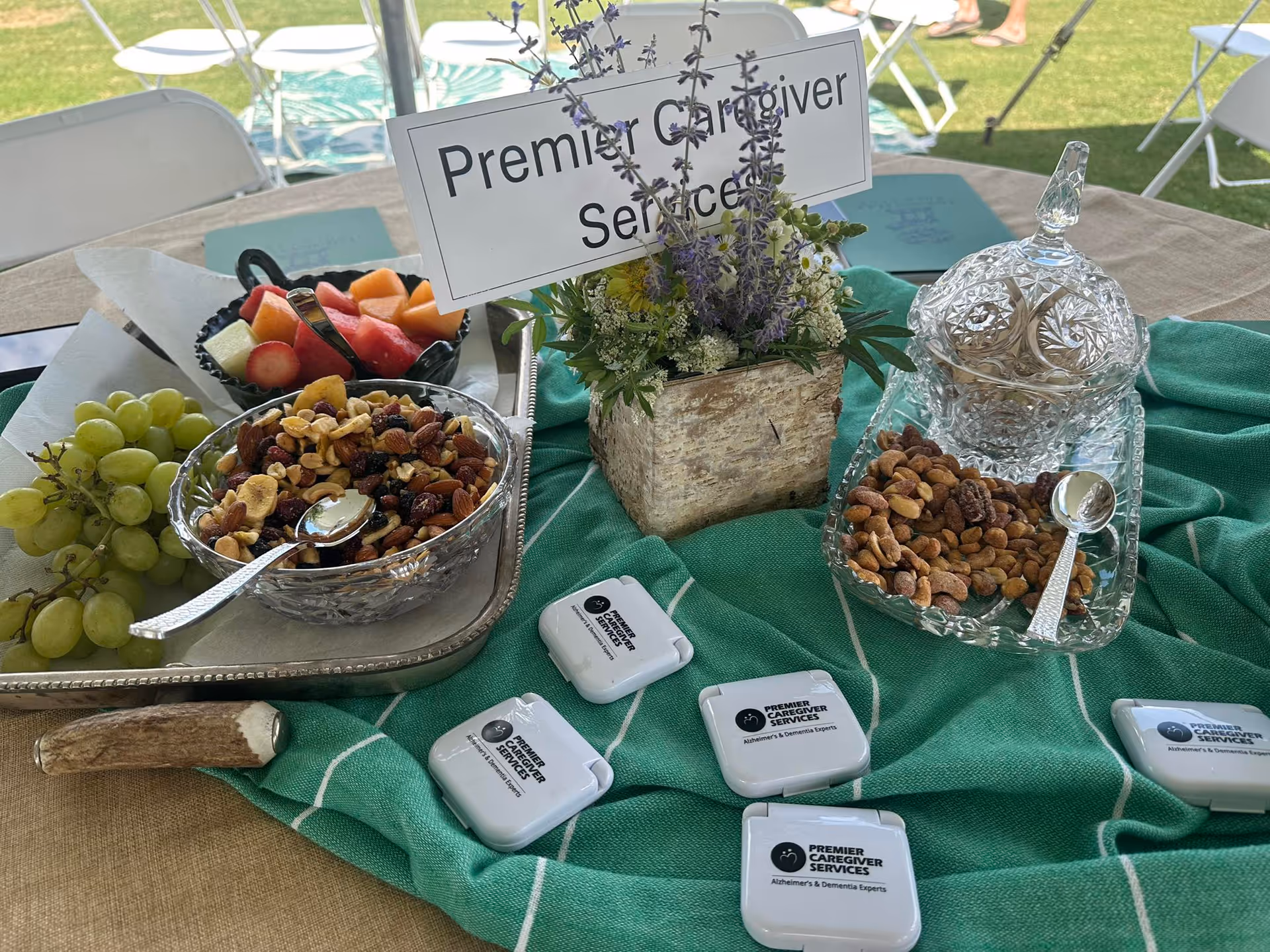 Outdoor event table displaying Premier Caregiver Services branding with bowls of nuts and fruit