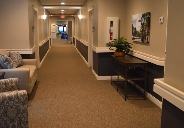 Wide beige hallway in a senior living facility with seating, plants, and wall art.