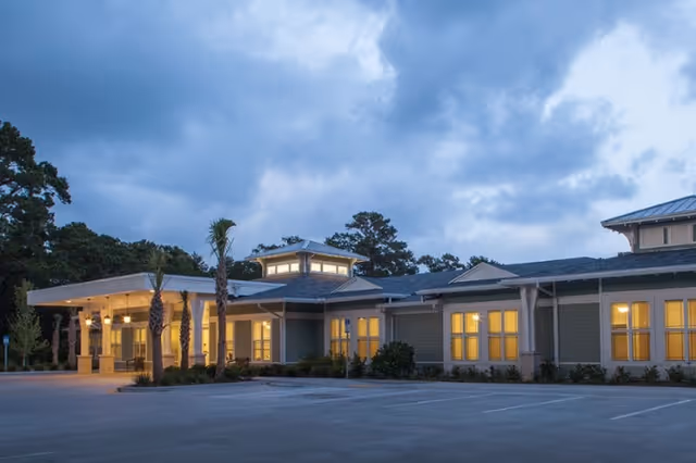 Exterior front of a single-story senior living building at dusk with illuminated windows and a covered entryway.