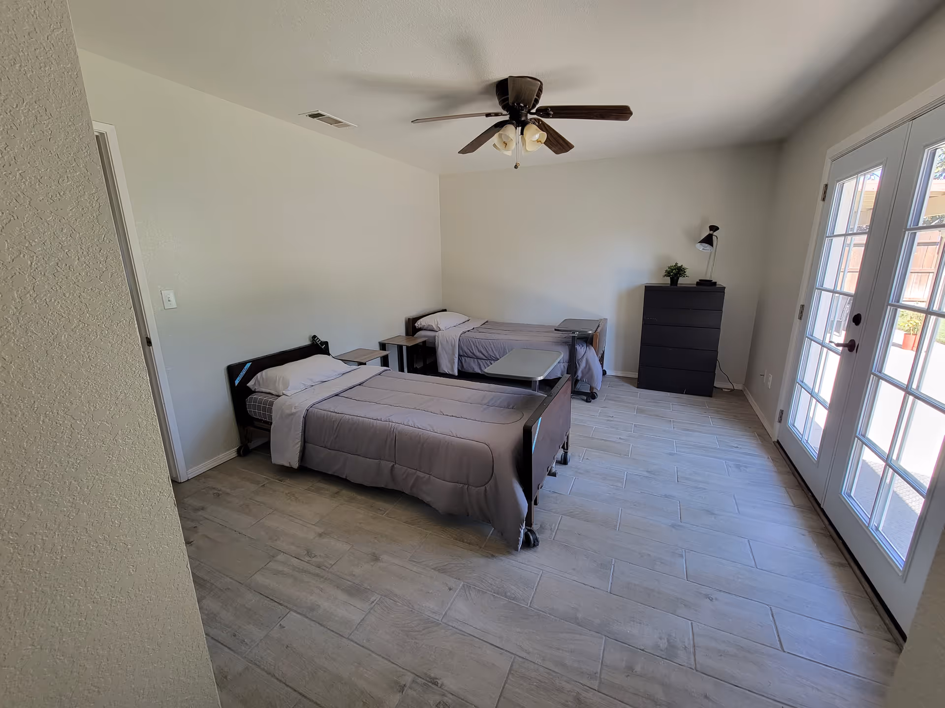 Bright shared bedroom with two twin beds, nightstands, a dresser, and glass doors.