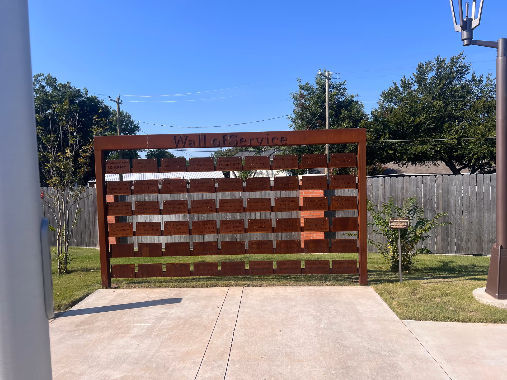 A wooden Wall of Service with many plaques stands in an open outdoor area.