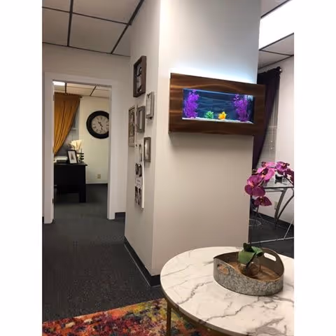 Hallway of a senior living facility with a wall-mounted fish tank, marble table, and office area.