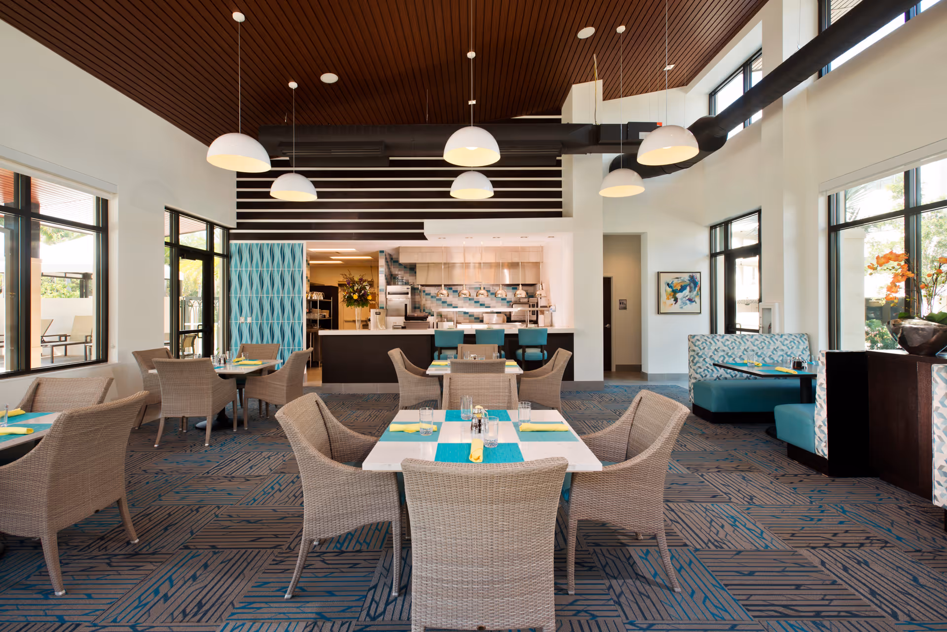 Interior dining area at Moorings Park at Grey Oaks, showcasing tables, chairs, and a visible kitchen.
