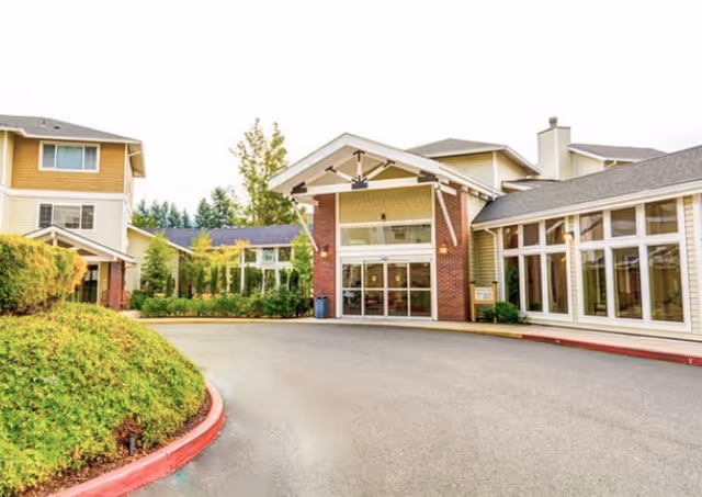 Exterior view of a senior living facility with curved driveway and glass entrance.