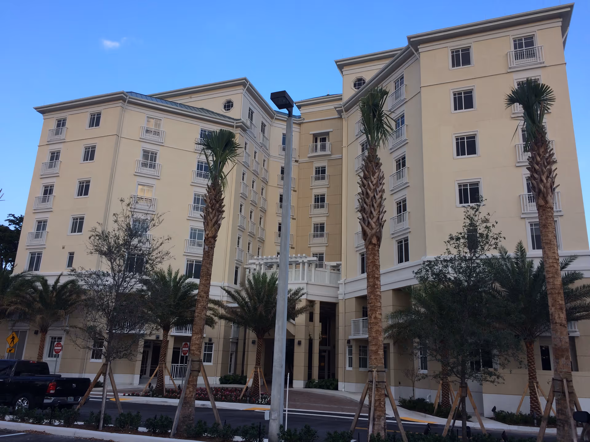 Exterior view of a multi-story senior living building with palm trees and a driveway.
