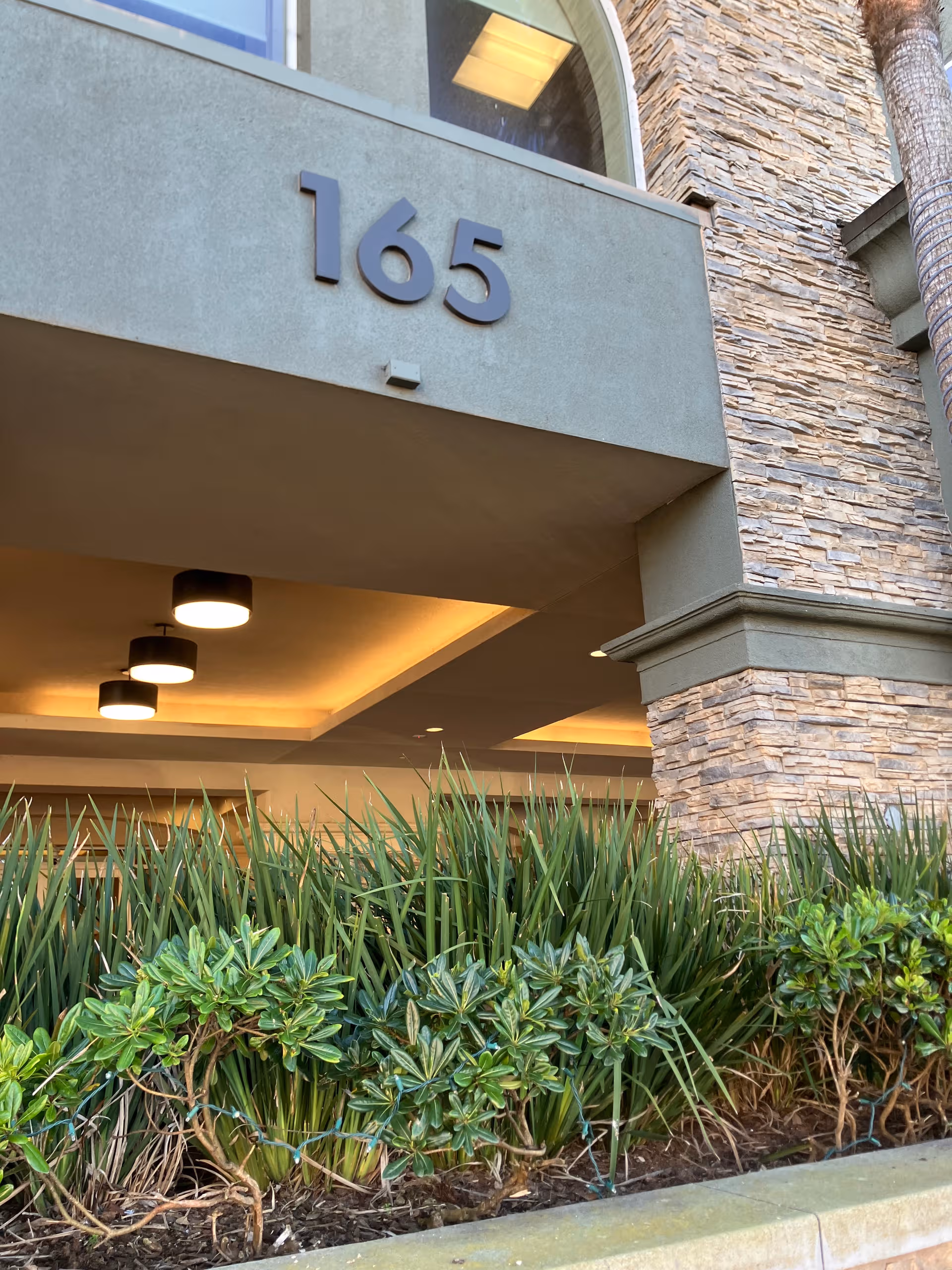 Entrance of Peninsula Del Rey with the numbers 165, stone facade, and landscaping.