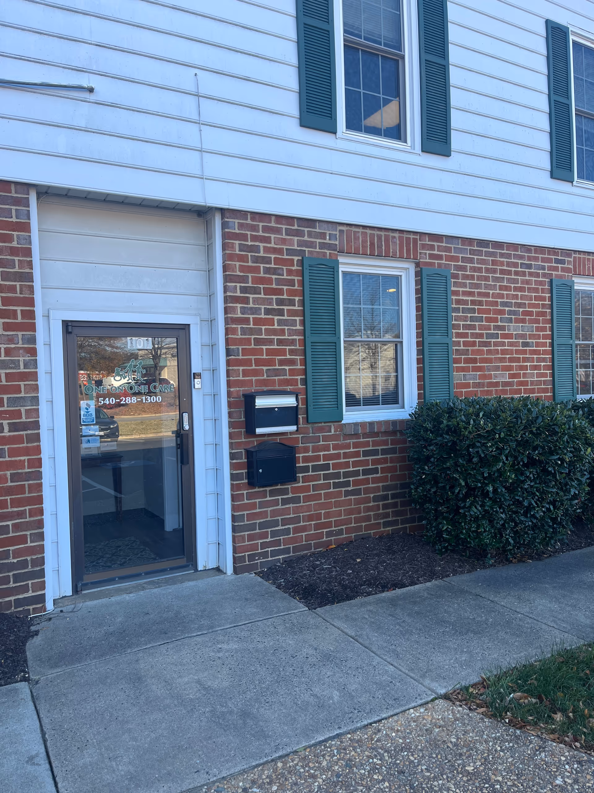 Brick exterior of a senior care facility with a glass door entrance and green shutters.