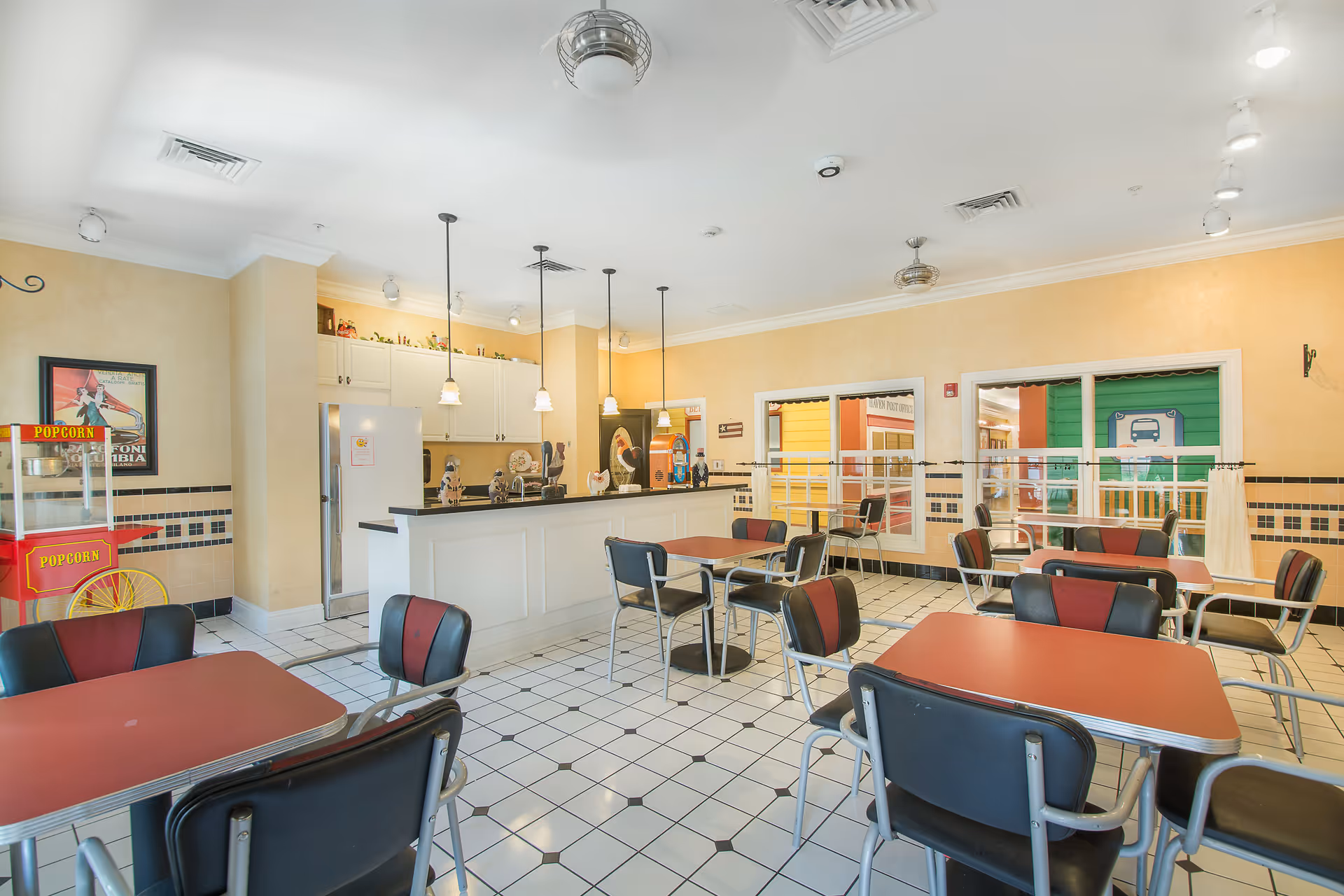 Bright, retro-style dining hall with red tables, black chairs, and a service counter.