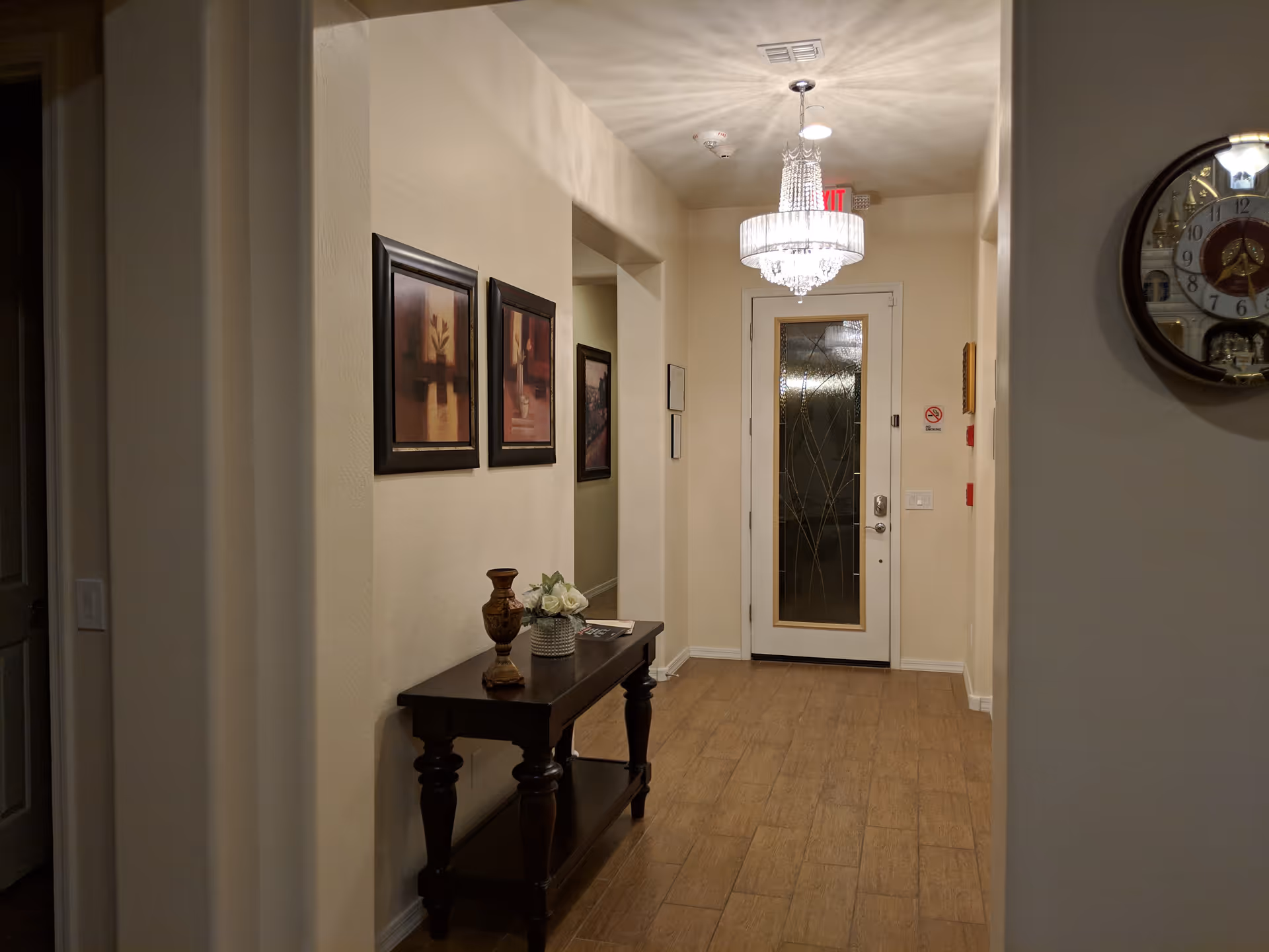 Hallway of a senior living facility with a glass door, chandelier, and framed art.