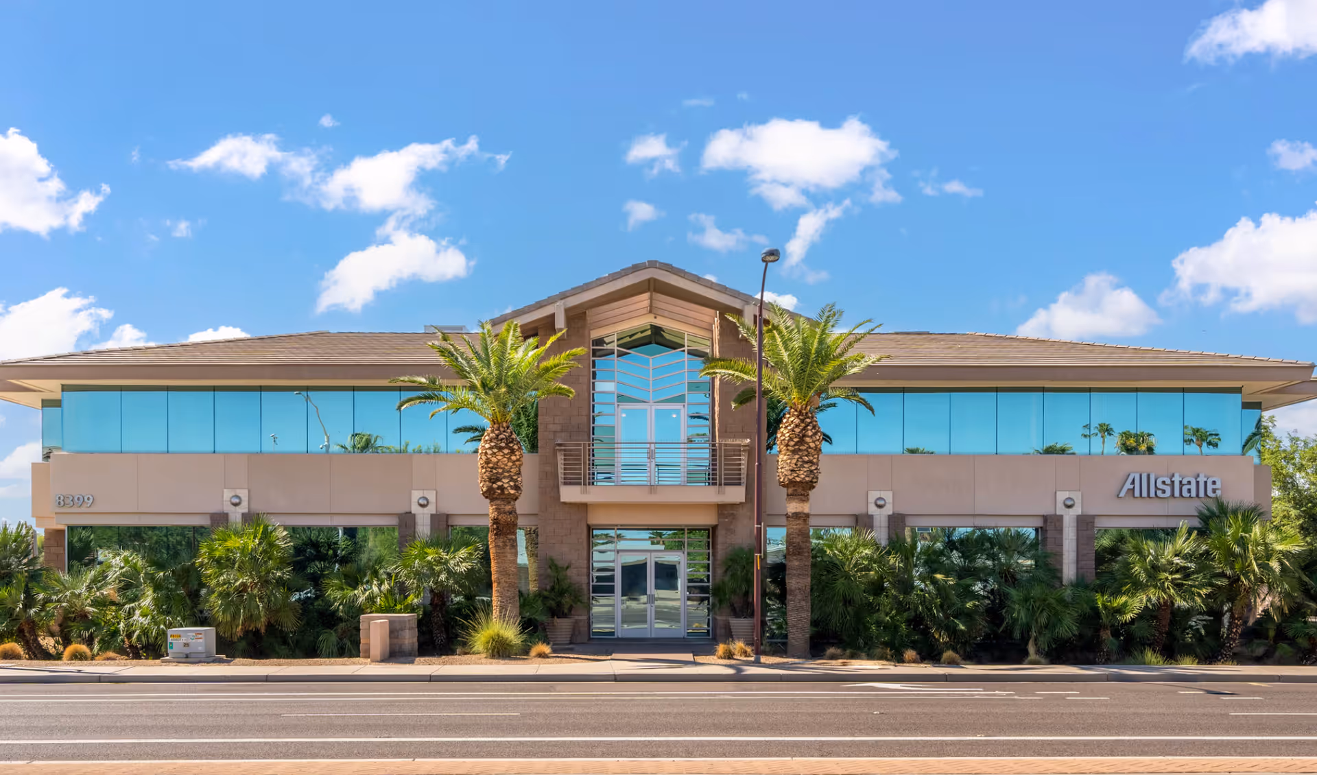 Modern, single-story building façade with glass windows, palm trees, and a central entrance.