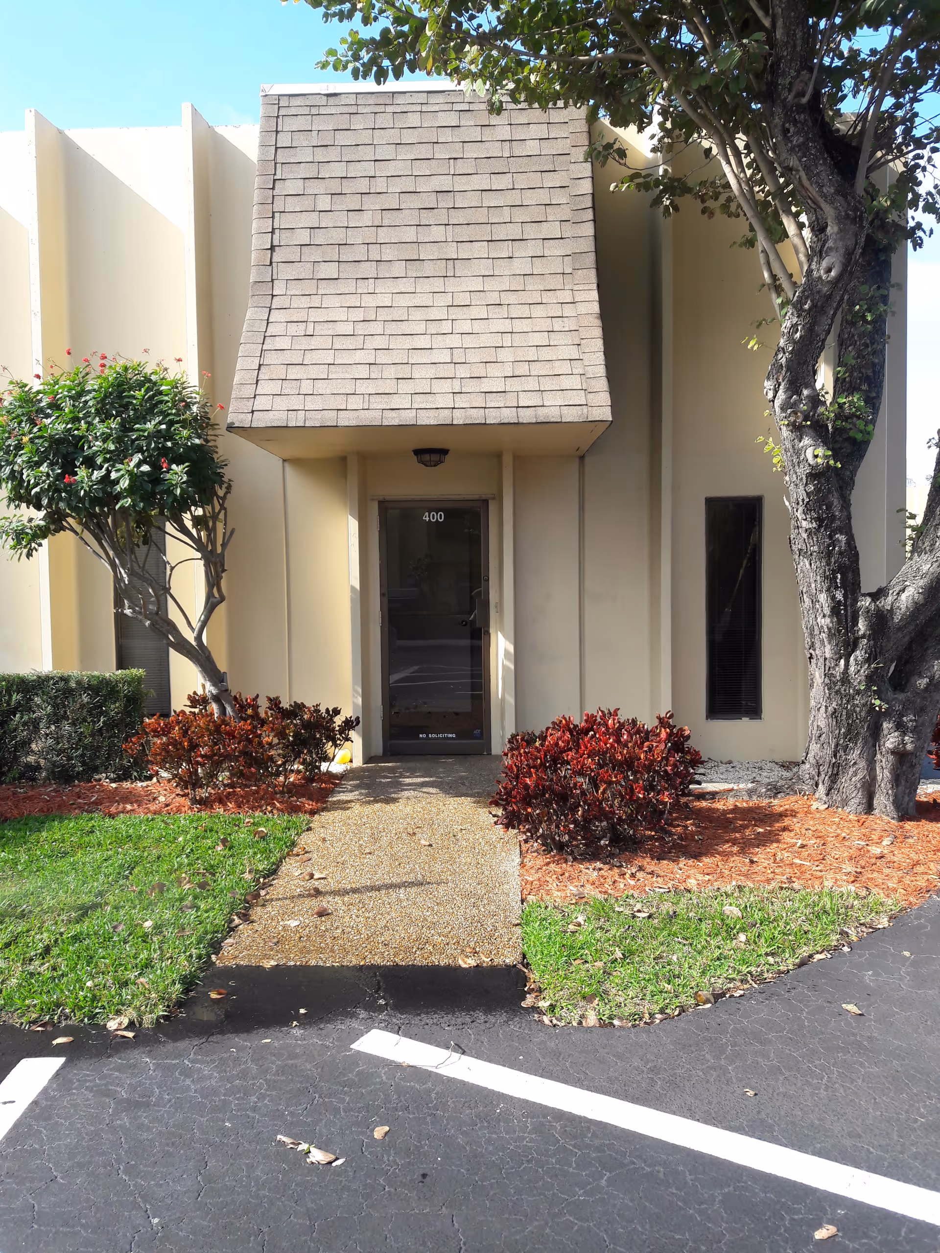 Beige building exterior with glass door entrance marked 400, flanked by trees and shrubs.