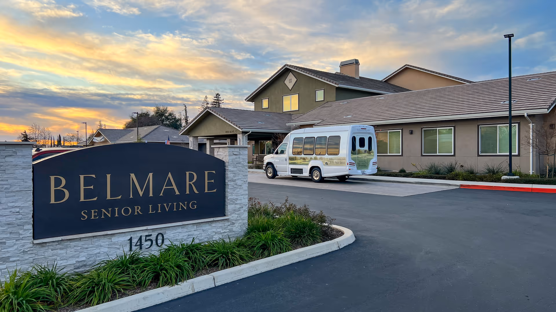 Belmar Senior Living sign in foreground with a beige building and a white shuttle bus.