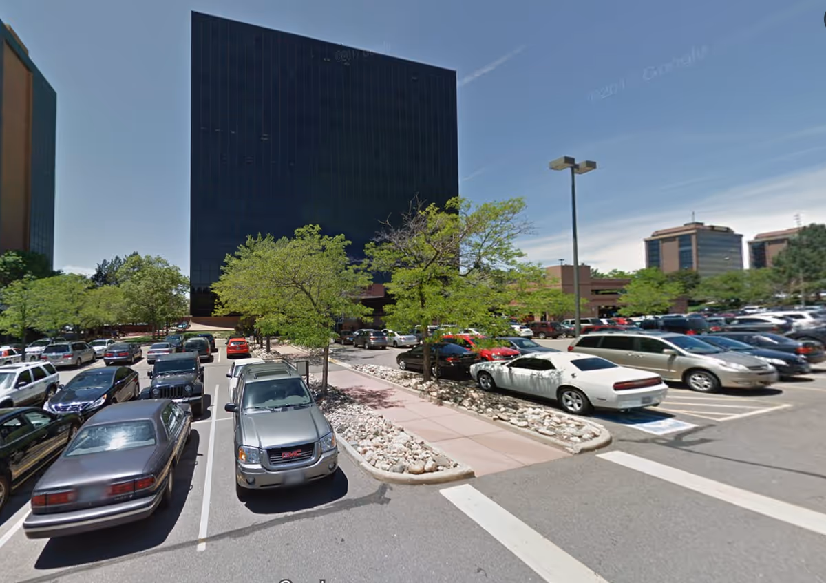 Parking lot in front of a tall dark office building with trees.