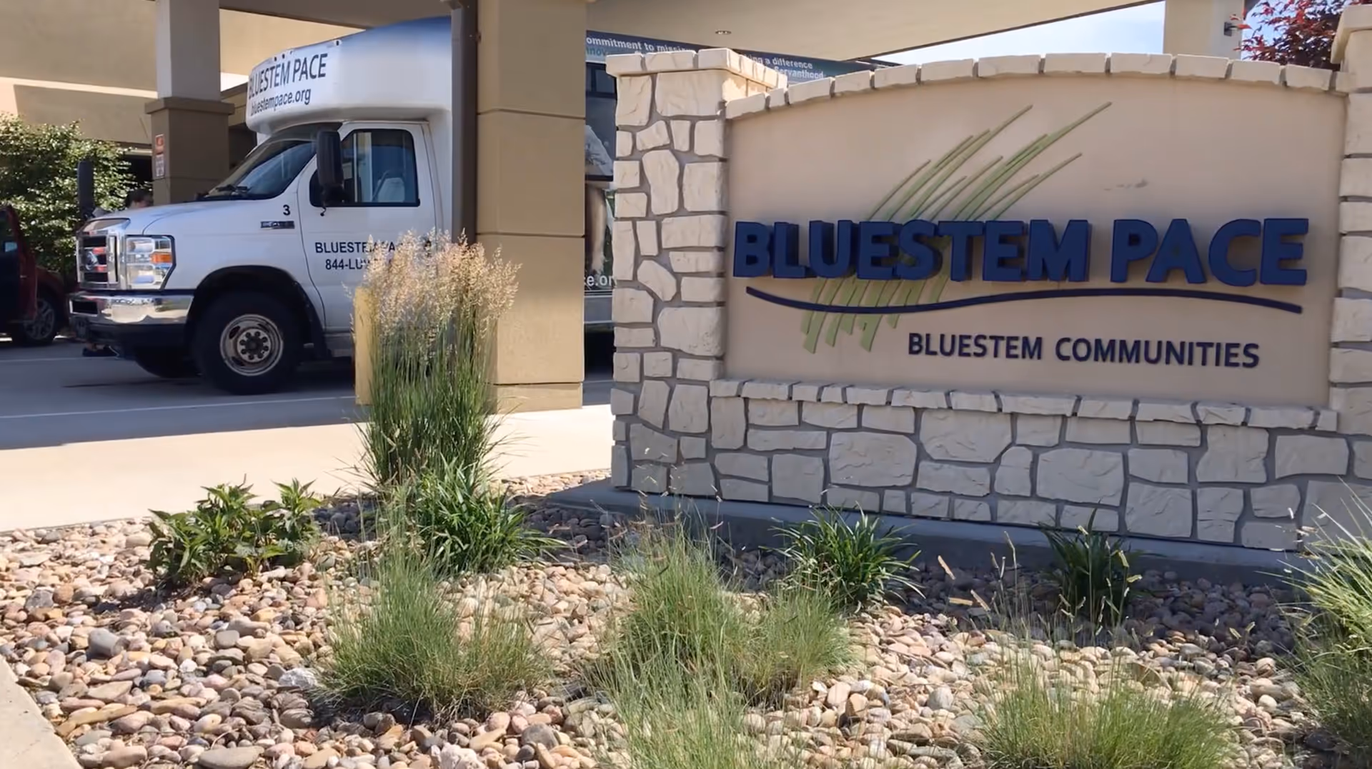 Exterior view of Bluestem PACE entrance with stone sign and a parked service van.