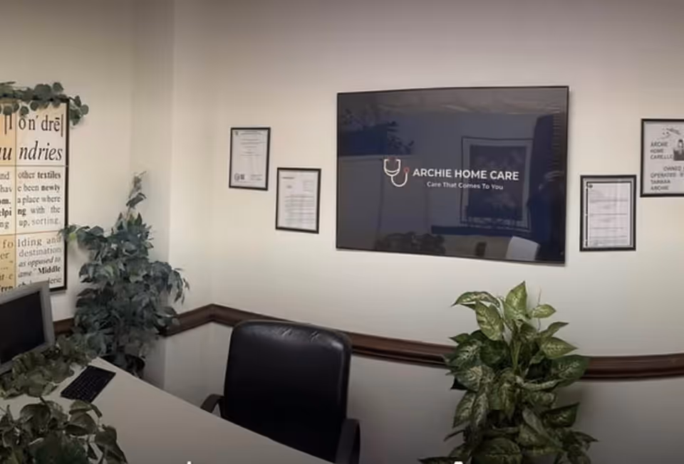 Reception area featuring a wall screen displaying Archie Home Care, framed certificates, and plants.