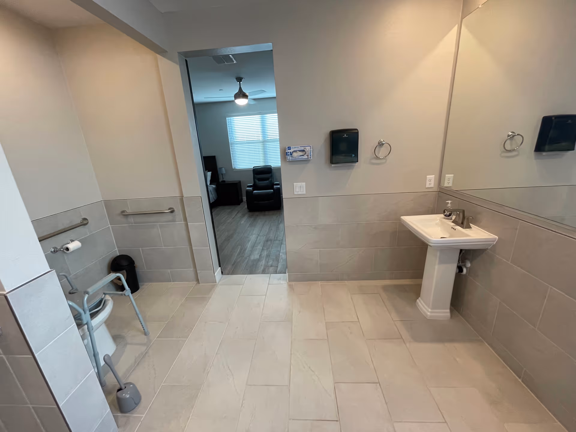 Accessible bathroom with grab bars, a toilet, and pedestal sink near doorway.
