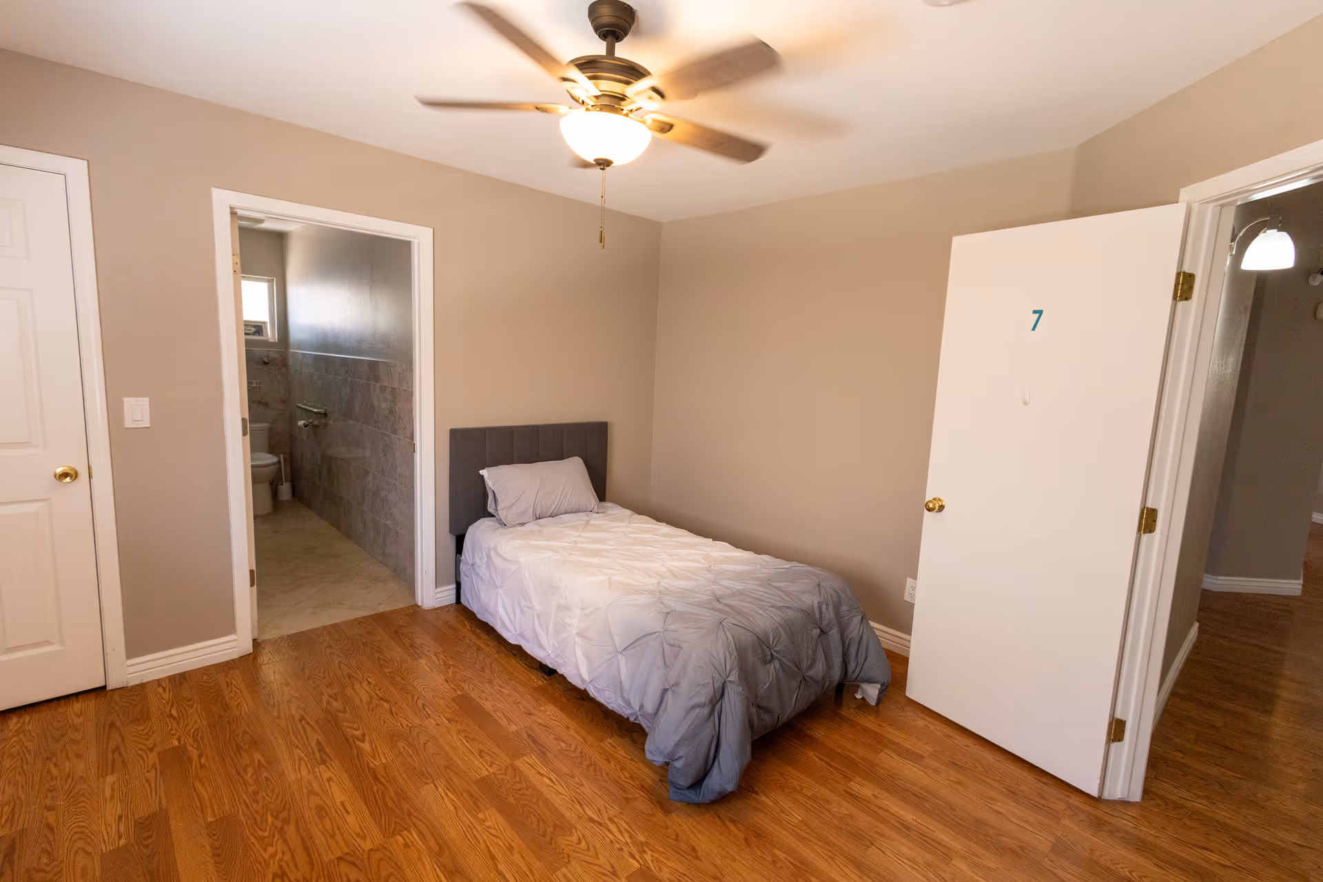 Bedroom with single bed, ceiling fan, numbered door, and adjoining bathroom.