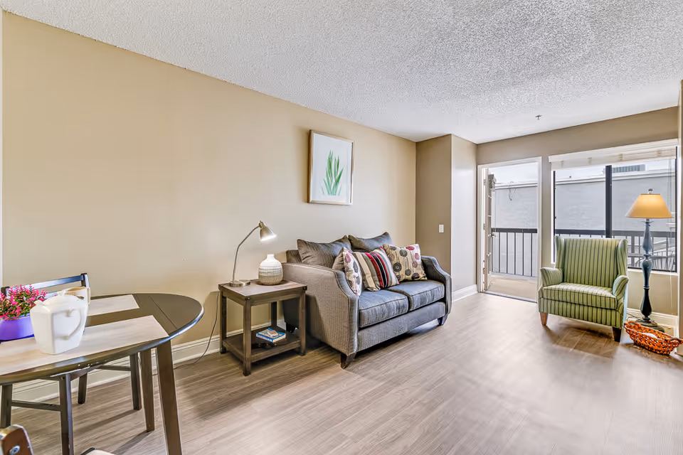 Bright living room with sofa, chair, coffee table, and balcony doors.