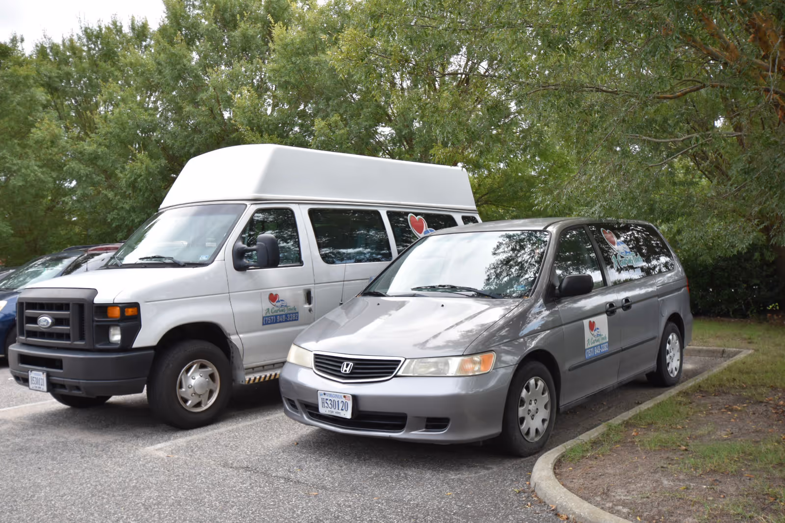 Two service vans with heart logos parked in a tree-lined outdoor lot.