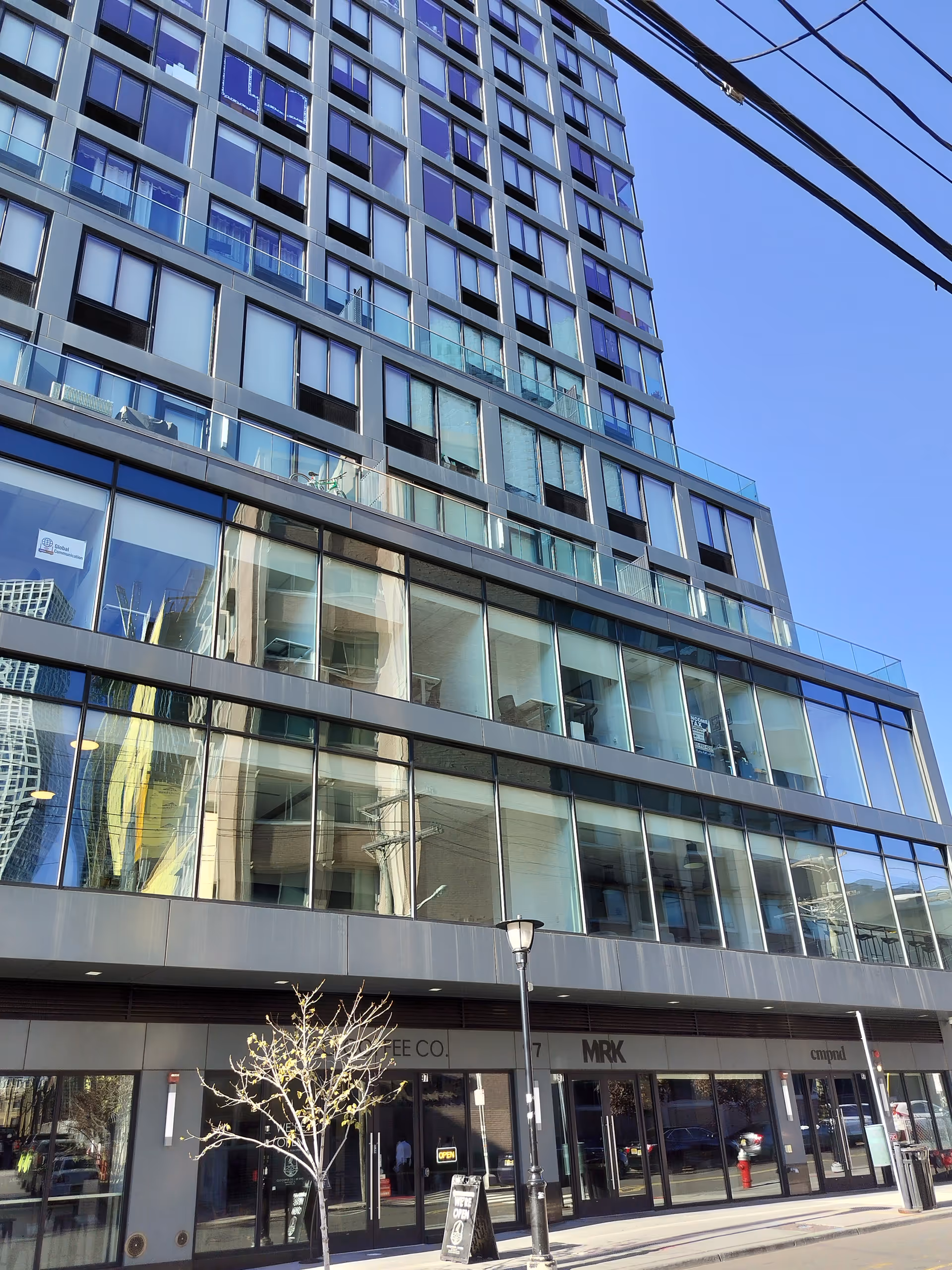 Modern glass-fronted high-rise building with storefronts along a city street.